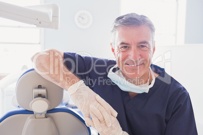 Smiling dentist leaning against dentists chair