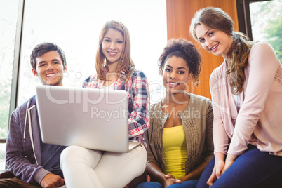 Smiling students sitting on couch using laptop