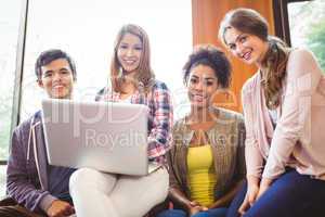 Smiling students sitting on couch using laptop