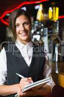 Happy barmaid smiling at camera taking notes
