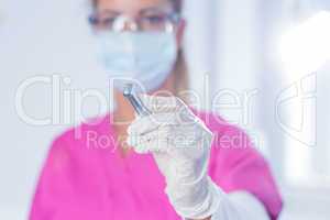 Dentist in surgical mask and scrubs holding tool