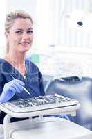 Dentist sitting with tray of tools smiling at camera