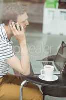 Smiling student using laptop and smartphone in cafe