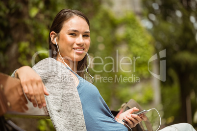 Smiling student sitting on bench listening music with mobile pho