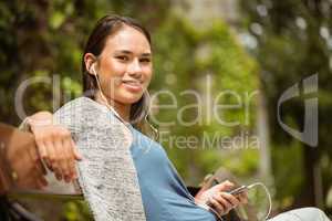 Smiling student sitting on bench listening music with mobile pho