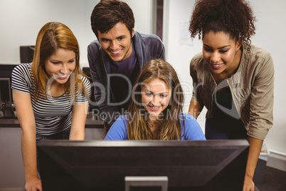 Smiling students sitting at desk using computer together
