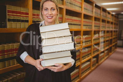 Smiling lawyer holding heavy pile of books standing