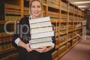 Smiling lawyer holding heavy pile of books standing