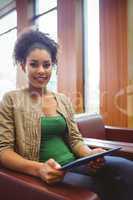 Student sitting on sofa using her tablet pc smiling at camera