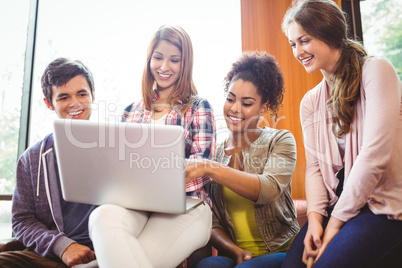 Smiling students sitting on couch using laptop