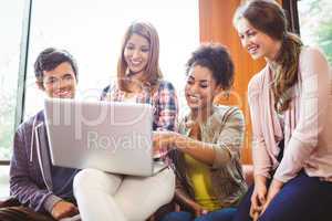 Smiling students sitting on couch using laptop