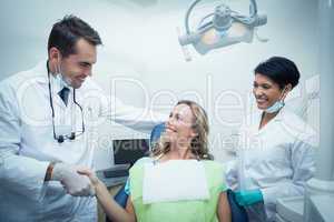 Male dentist with assistant shaking hands with woman