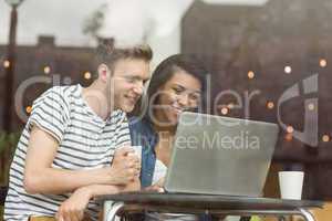 Smiling friends with a hot drink using laptop