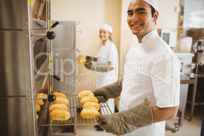 Baker smiling at camera taking rolls out of oven