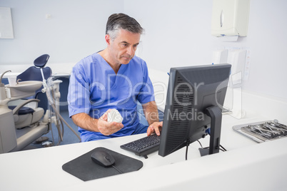 Serious dentist using computer and holding model