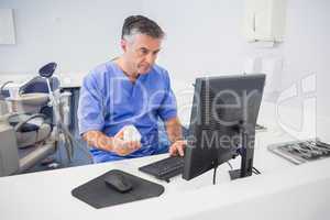 Serious dentist using computer and holding model