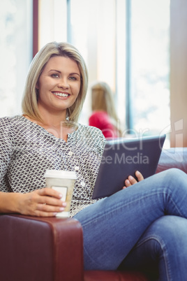 Smiling girl using digital tablet and holding disposable cup