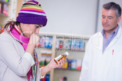Sick girl with scarf and colorful hat holding a bottle of drug