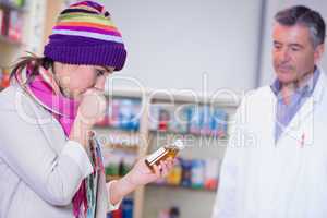 Sick girl with scarf and colorful hat holding a bottle of drug