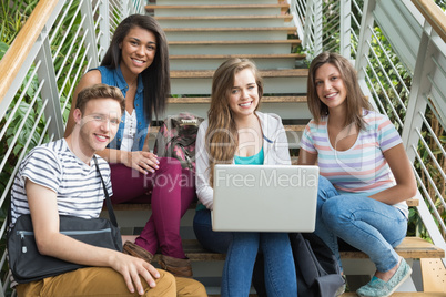 Smiling students sitting on steps with laptop