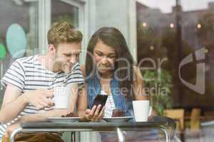 Smiling friends with chocolate cake using smartphone