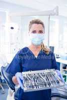 Dentist in blue scrubs offering tray of tools