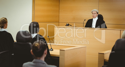 Unsmiling judge wearing wig with american flag behind him