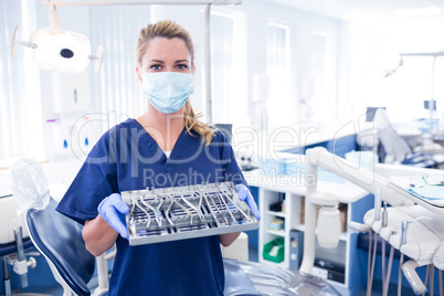 Dentist in blue scrubs holding tray of tools