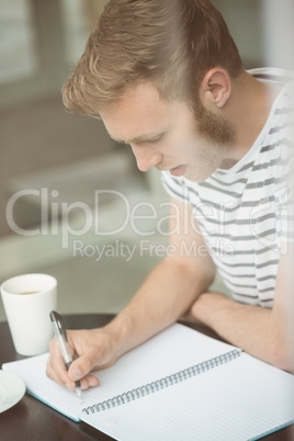 Smiling student sitting with a hot drink and writing on notepad