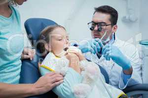 Dentist examining girls teeth with assistant