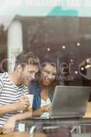 Smiling friends with a hot drink using laptop