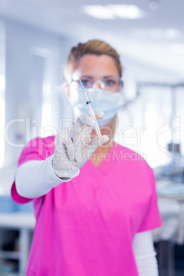 Dentist in surgical mask and scrubs holding syring