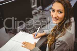 Smiling student sitting at desk writing on notepad