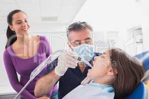 Pediatric dentist examining young patient with a suction tube