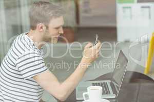 Smiling student using laptop and smartphone in cafe