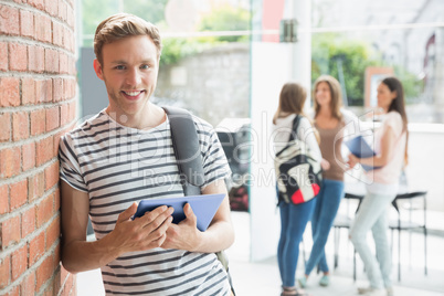 Handsome student smiling and holding tablet