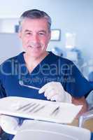 Dentist in blue scrubs smiling at camera holding tools