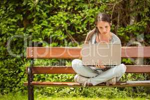 Student sitting on bench listening music and using laptop