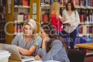 Two focused students on laptop with classmates behind them