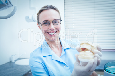 Smiling female dentist holding mouth model