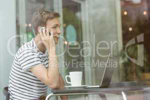 Smiling student using laptop and smartphone in cafe