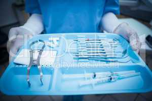 Mid section of dentist in blue scrubs holding tray of tools