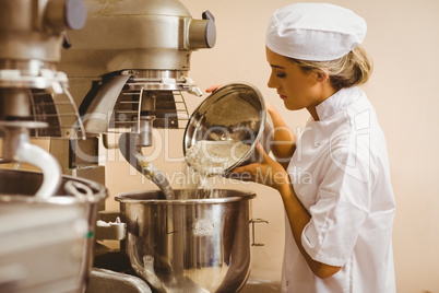 Baker pouring flour into large mixer