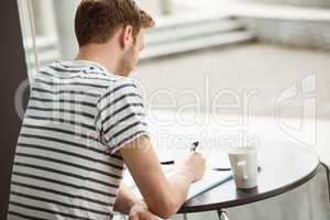 Student sitting with a hot drink and writing on notepad