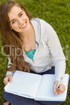 Smiling university student sitting and writing on notepad