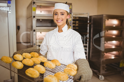 Baker smiling at camera holding rack of rolls