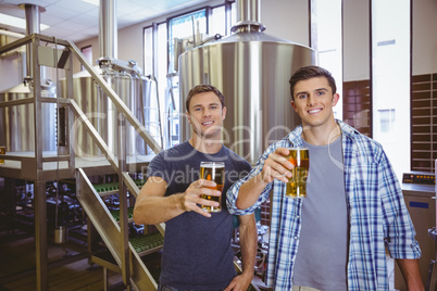 Young men holding a pint of beer smiling at camera