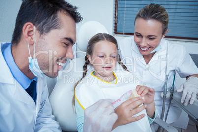 Dentist with assistant teaching girl how to brush teeth