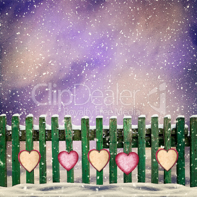 snow-covered wooden fence with hanging on it with paper hearts