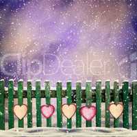 snow-covered wooden fence with hanging on it with paper hearts